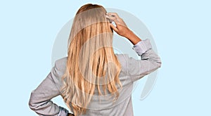 Beautiful blonde young woman wearing business clothes backwards thinking about doubt with hand on head