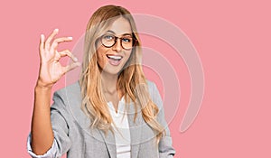 Beautiful blonde young woman wearing business clothes smiling positive doing ok sign with hand and fingers