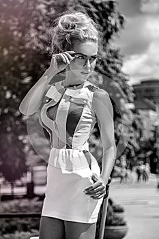 Beautiful blonde young woman wearing sunglasses, and dress walking on the street.