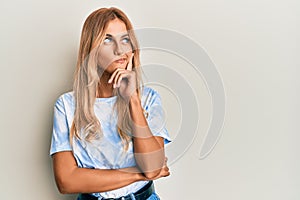 Beautiful blonde young woman wearing tye die tshirt thinking concentrated about doubt with finger on chin and looking up wondering