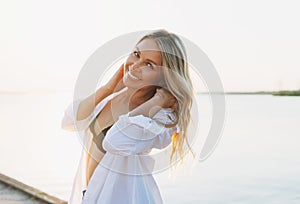 Beautiful blonde young woman in white shirt on pier on sunset