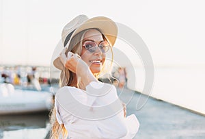 Beautiful blonde young woman in white shirt and straw hat on the pier on sunset