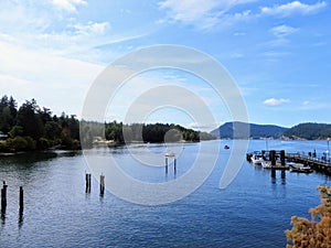 A beautiful blue bay with wooden jetties and a dock with boats surrounded by forested islands on Mayne Island, British Columbia