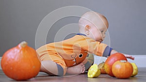 beautiful blue eyed baby in orange clothes crawling away from pumpkins