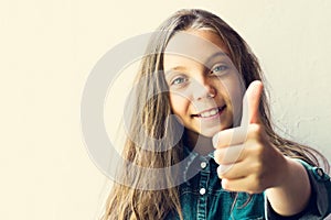 Beautiful blue-eyed, blonde girl teenager, in a denim shirt, with a thumb up. On a light background. Copy space. Close-up. Beauty