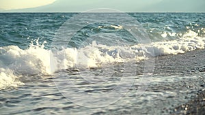 Beautiful blue foamy sea waves rolling crashing onto shore, pebble beach with clear azure water