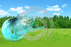 Beautiful blue globe, a model of the planet explodes in spray on a green landscape background, the concept of natural nature,