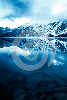 Beautiful blue lake in the mountains. Flat mirror surface of the water under the clouds. The beauty of winter nature.