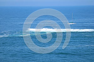 Beautiful blue ocean with the crashing waves and a white yacht