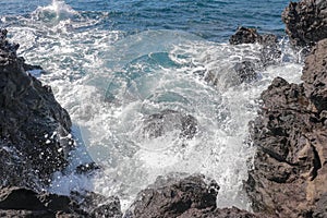 Beautiful blue sea and a beach with huge stone blocks. Danger sea wave crashing on rock coast with spray and foam. Stony coast