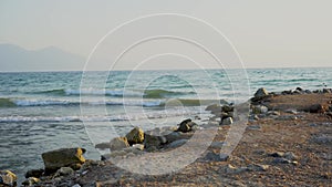 Beautiful blue sea and large calm waves float to stony beach. Ocean, mountains and sky background landscape on sunset