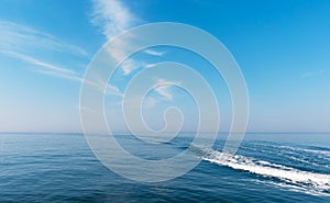 Beautiful blue sky with light white clouds. Boat cruising the sea leaving wake on a brilliant sunny day.