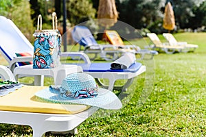 Beautiful blue straw hat on yellow sunbed near pool. Side View. Summer Travel Vacation Concept