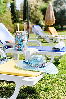 Beautiful blue straw hat on yellow sunbed near pool. Side View. Summer Travel Vacation Concept