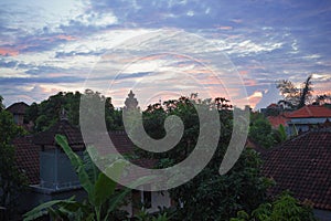 Beautiful blue twilight in Balinese village in the morning. Green trees and houses of countryside under blue sky with