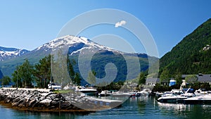 Beautiful boat marina harbor at Valldal, Norway on the calm waters of a fjord on a sunny day with snow on the peaks.