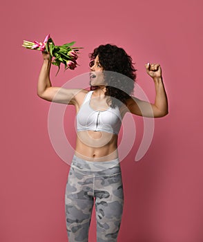 A beautiful body athletic girl with curly hair and in sportswear, holds in a strong muscular arm a bouquet of gentle tulpans