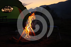 Beautiful bonfire and folding chairs near camping tent outdoors in evening