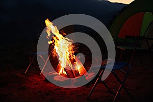 Beautiful bonfire and folding chairs near camping tent outdoors in evening