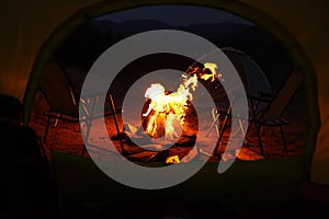 Beautiful bonfire and folding chairs outdoors in evening, view from camping tent