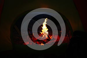 Beautiful bonfire and folding chairs outdoors in evening, view from camping tent