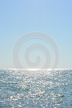 Beautiful border between the blue sky and the black sea with small waves and fine golden and bright reflections of the sun on the