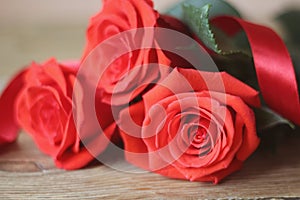 Beautiful bouguet red roses with green leaves and red satin ribbon lying on a wooden table. Macro.. Macro.