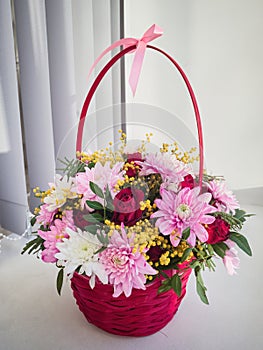 A beautiful bouquet of bright flowers in a wicker red basket stands on the window on a white background