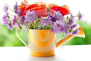 Beautiful bouquet of bright wildflowers in yellow watering can on white wooden background