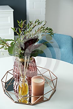 Beautiful bouquet with eucalyptus branches, candle and aromatic reed air freshener on white table indoors. Interior elements