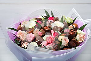 Beautiful bouquet of flowers and chocolate candies on light background, closeup