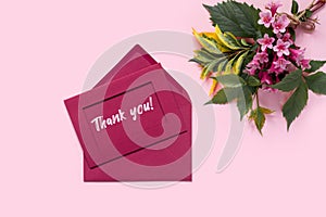 Beautiful bouquet of flowers of delicate weigela on pink background. Envelope and letter with the inscription Thank you! Minimal