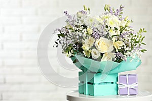 Beautiful bouquet of flowers and gift box on table against light background.