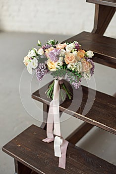 Beautiful bouquet of flowers of roses and lilac stands on a wooden ladder against a white brick wall.