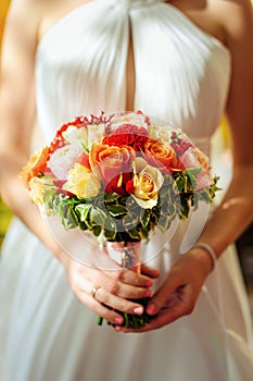 Beautiful bouquet of fresh flowers in the hands of bride in white dress. Wedding flowers close-up