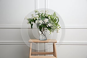 Beautiful bouquet with fresh jasmine flowers in vase on wooden table indoors
