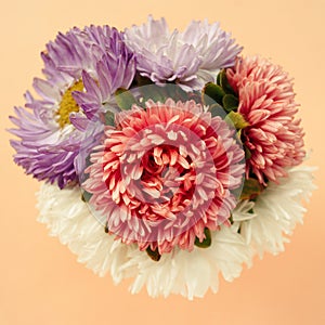 Beautiful bouquet of pink, lilac, white aster on a pale peach pastel background.