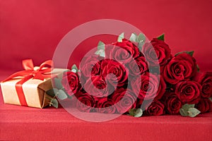 Beautiful bouquet of red roses with gift box on the red background - greeting card concept