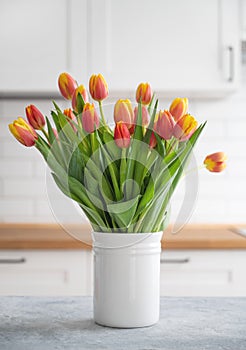 A beautiful bouquet of red and yellow tulips in a white vase on a blue wooden countertop against a white kitchen background.