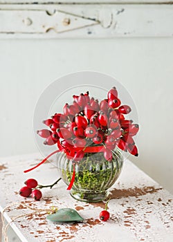 Beautiful bouquet of rose hips in vintage glass vase as autumn decoration.