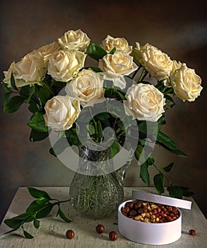 A beautiful bouquet of roses in a crystal jug and a box with tasty nuts.