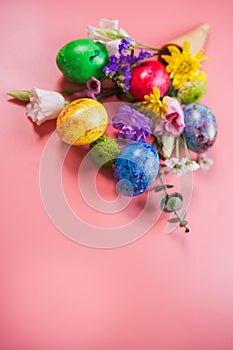 Beautiful bouquet of spring flowers and easter eggs in ice cream cone on pink background.