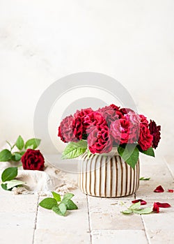 Beautiful bouquet of summer dark red roses in ceramic vase on light stone mosaic background.
