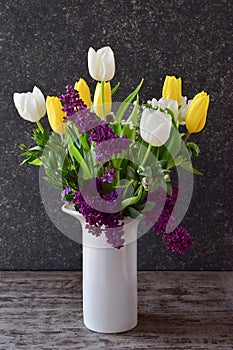 A beautiful bouquet of tulips and lilacs in a white vase, side view