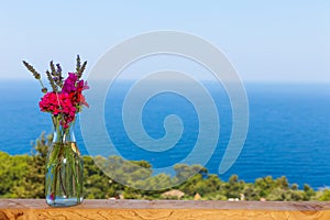 Beautiful bouquet in vase on wooden hand rail against seascape background