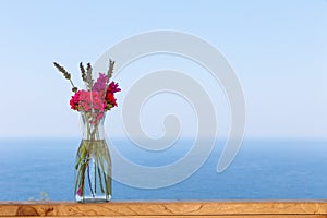 Beautiful bouquet in vase on wooden hand rail against seascape background