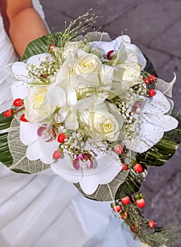 Beautiful bouquet of white roses with orchids and red berries held by a bride`s hand on her wedding day. Roses, Orchidaceae.