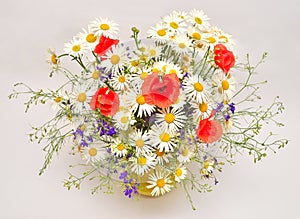 Beautiful bouquet of wild flowers daisies, poppies and consolida regalis in a vase on white background