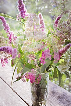 A beautiful bouquet of wild flowers on a wooden surface in the rays of the setting sun. Summer, nature, beauty. Vertical