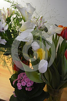 Beautiful bouquets in jars, glass glasses, bottles placed on a yellow wooden table.